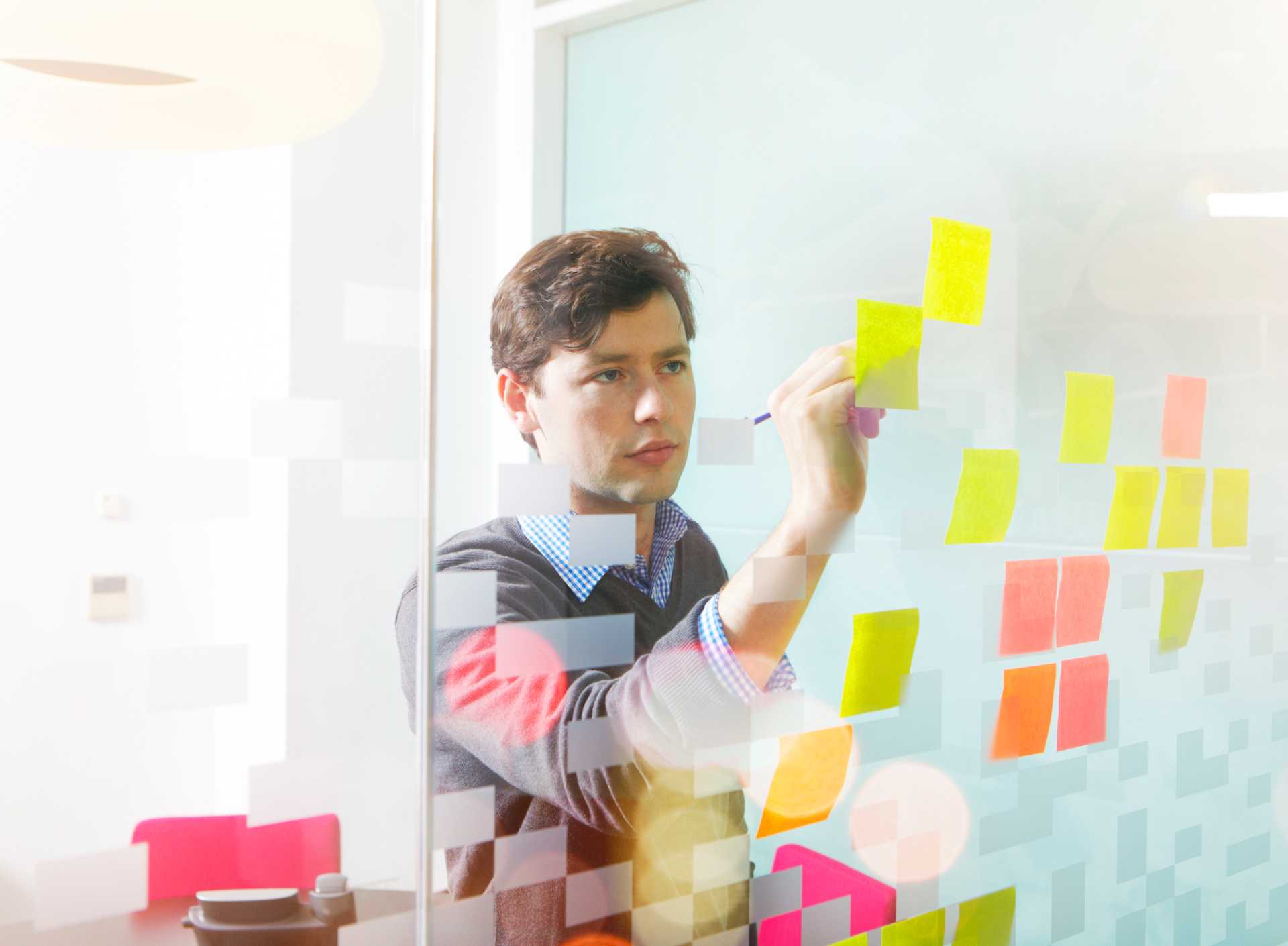 gestão à vista - gestor da empresa atualizando dados em post-its colados numa parede de vidro