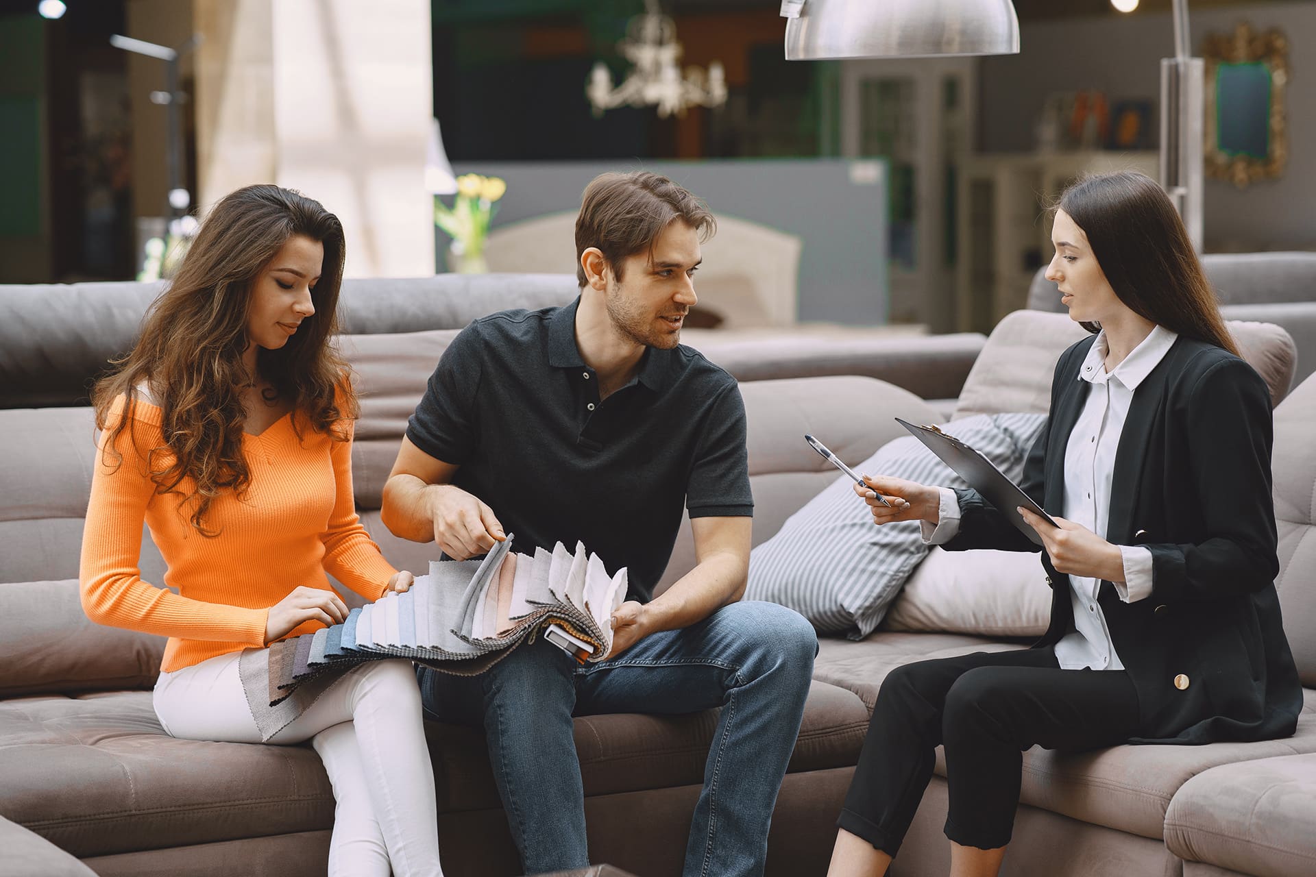necessidades do cliente - homem e mulher sentados lado a lado escolhendo amostras junto com a vendedora em uma loja de móveis