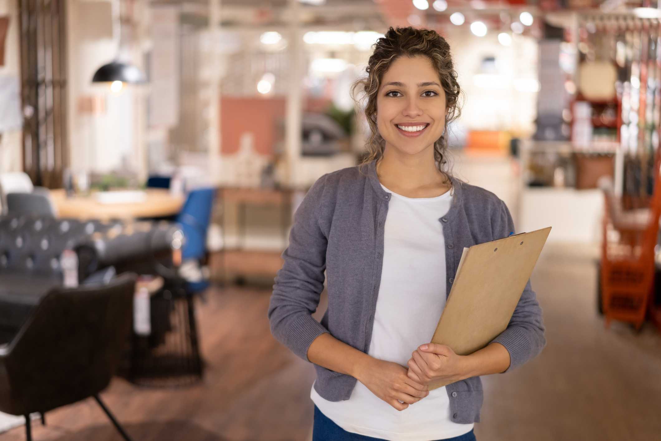 venda técnica - vendedora em uma loja de móveis sorrindo segurando uma prancheta